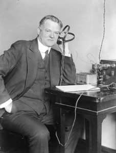 Herbert Hoover, three-quarter length portrait, seated, facing slightly right, listening to radio.