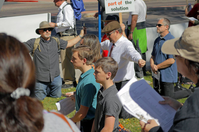 Men knelt to pray the rosary with their arms in the form of a cross.